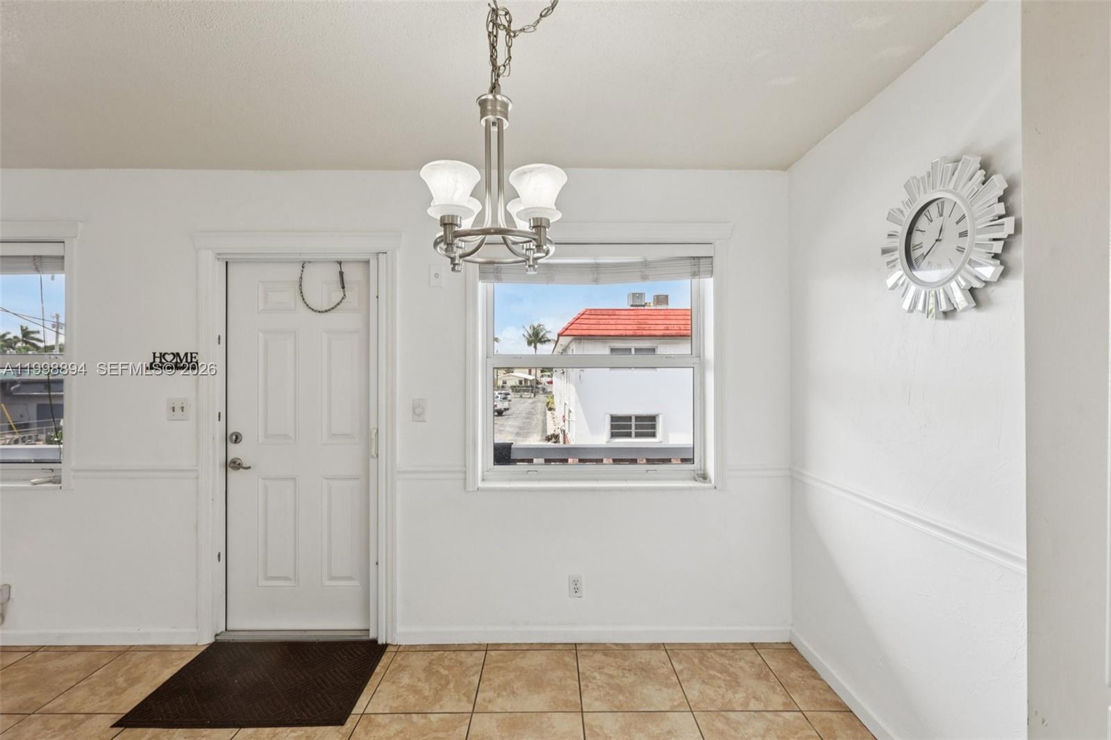 A dining area features a white door, a window, a chandelier, and a wall clock — 22 SE 3rd Ter # 18, Dania Beach FL 33004, DANIA BEACH, FL