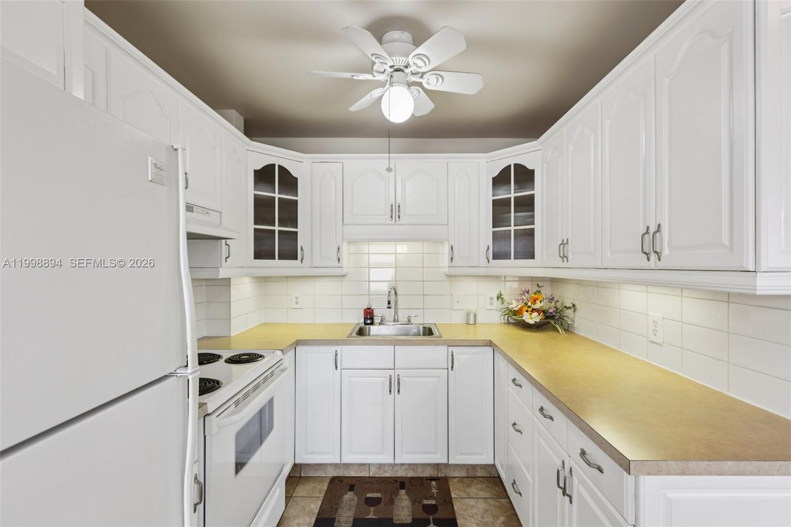 A white kitchen features a U-shaped layout, light countertops, and a ceiling fan — 22 SE 3rd Ter # 18, Dania Beach FL 33004, DANIA BEACH, FL