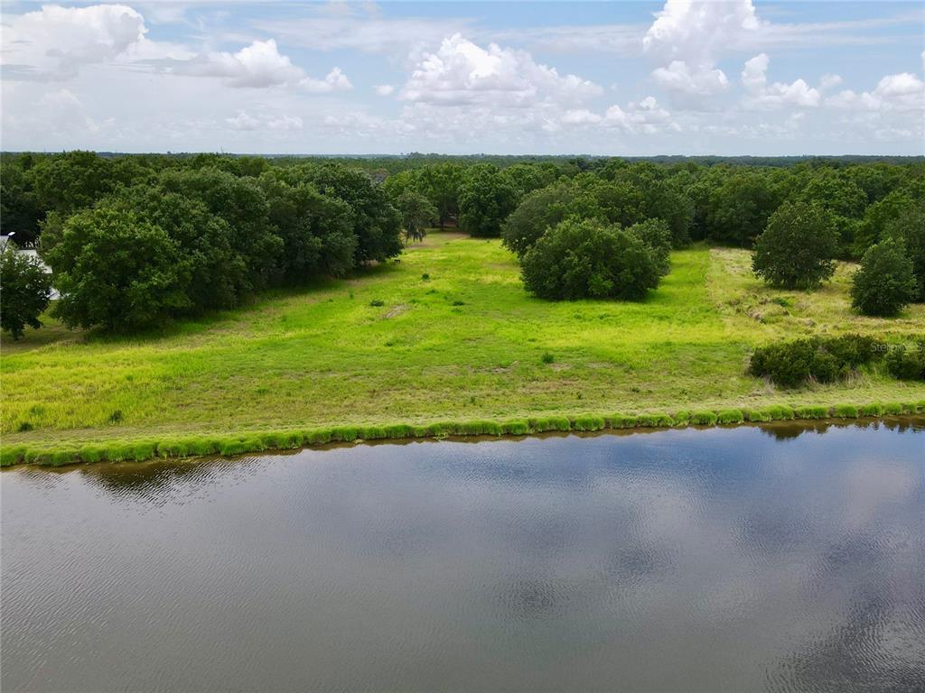 An aerial view of a grassy field bordering a calm pond under a cloudy sky — 4946 WAUCHULA RD, MYAKKA CITY, FL
