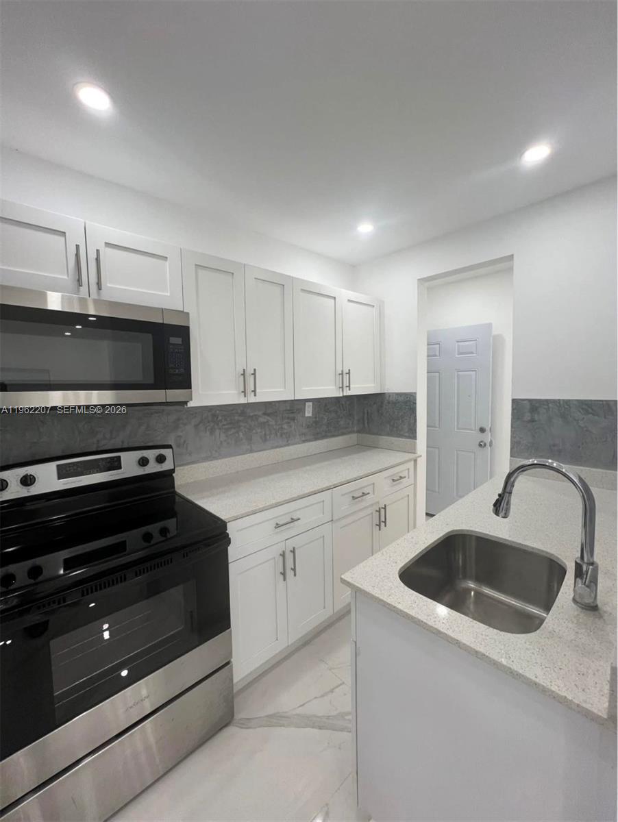 A kitchen features white cabinets, stainless steel appliances, a gray backsplash, and a sink island — 1015 S 17th Ave # 8, Hollywood FL 33020, HOLLYWOOD, FL