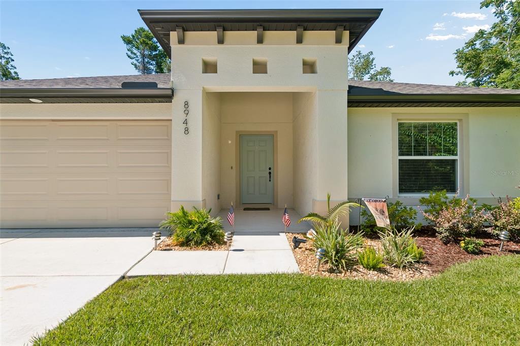 A single-story house exterior features a light-colored stucco facade, a garage, and a recessed entryway — 8948 CARRIE WAY, WEEKI WACHEE, FL