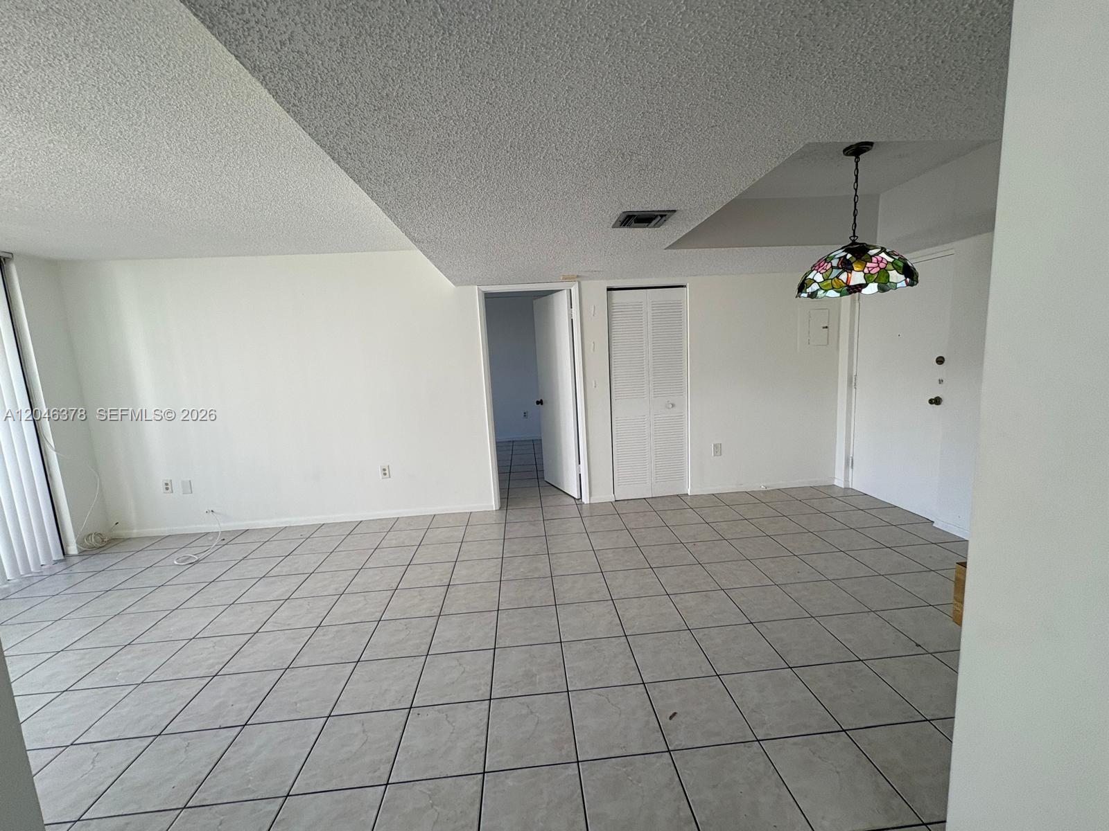 An empty room features white walls, light-colored tile flooring, and a stained-glass pendant light — 8004 SW 149th Ave # C205, Miami FL 33193, MIAMI, FL