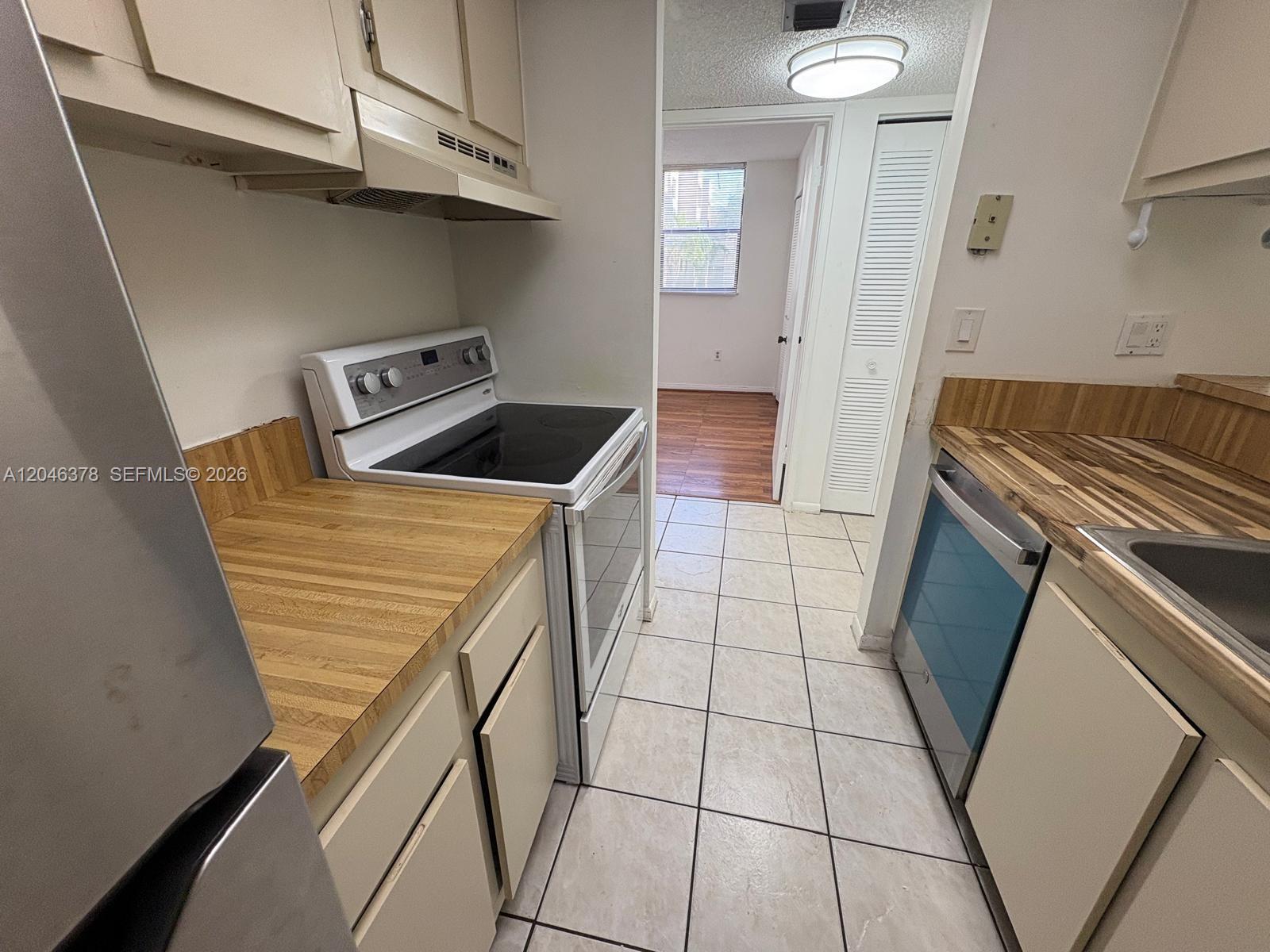 A galley kitchen features light-colored cabinets, wood-look countertops, a white stove, and tile flooring — 8004 SW 149th Ave # C205, Miami FL 33193, MIAMI, FL