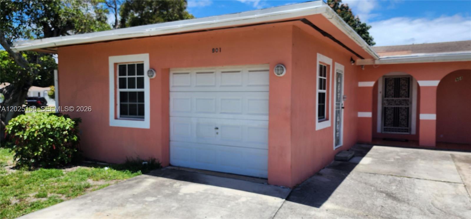 A peach-colored house exterior features a white garage door, a front entrance, and windows — 901 NE 160th Ter, North Miami Beach FL 33162, NORTH MIAMI BEACH, FL