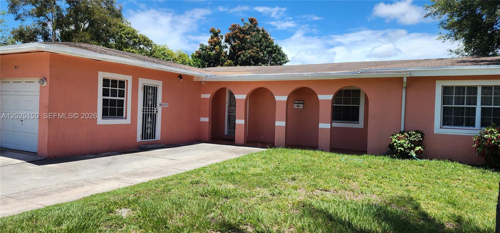A peach-colored single-story house features a garage, a covered arched entryway, and a lawn — 901 NE 160th Ter, North Miami Beach FL 33162, NORTH MIAMI BEACH, FL