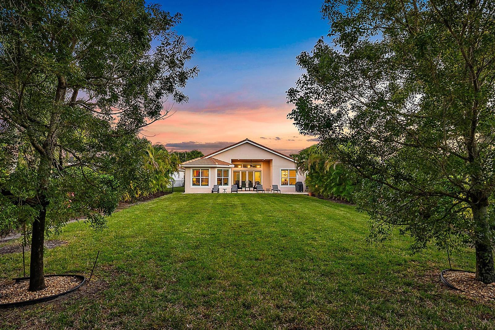 A view of a house exterior with a large backyard lawn framed by two trees — 271 Carina Drive, Jupiter FL 33478, JUPITER, FL