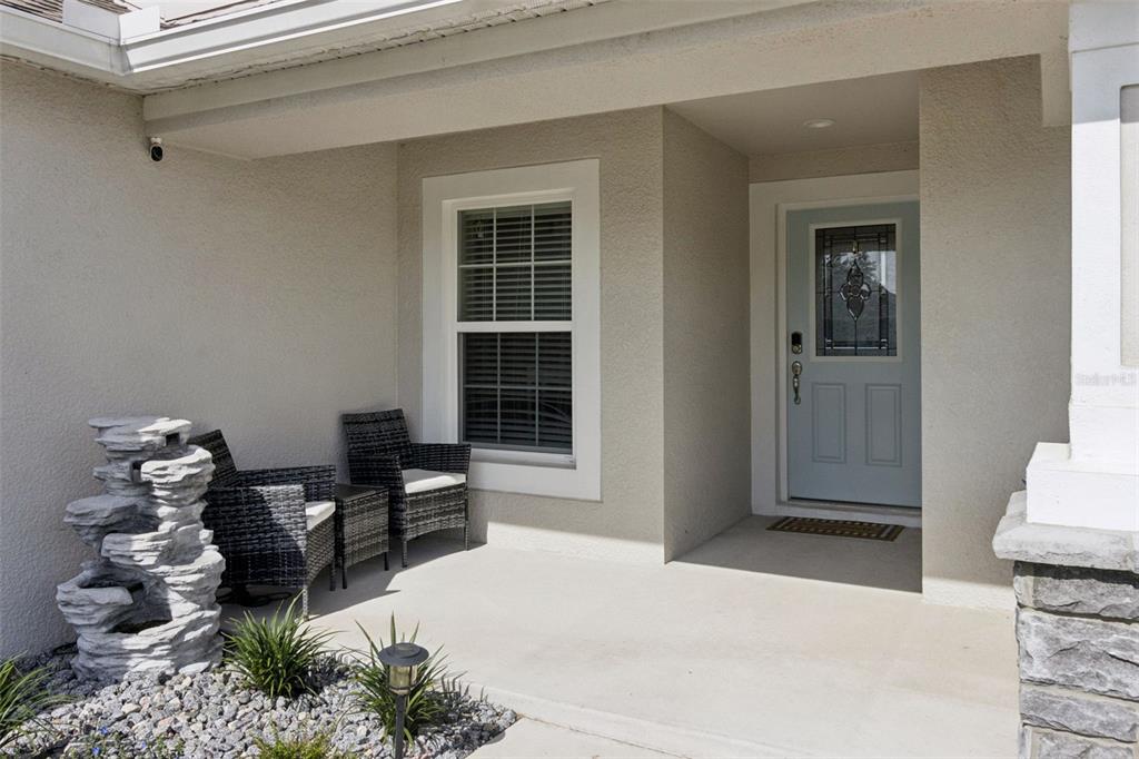 A covered front porch features a light blue door, two wicker chairs, and a stone fountain — 925 LOCHLAND LOOP, BARTOW, FL