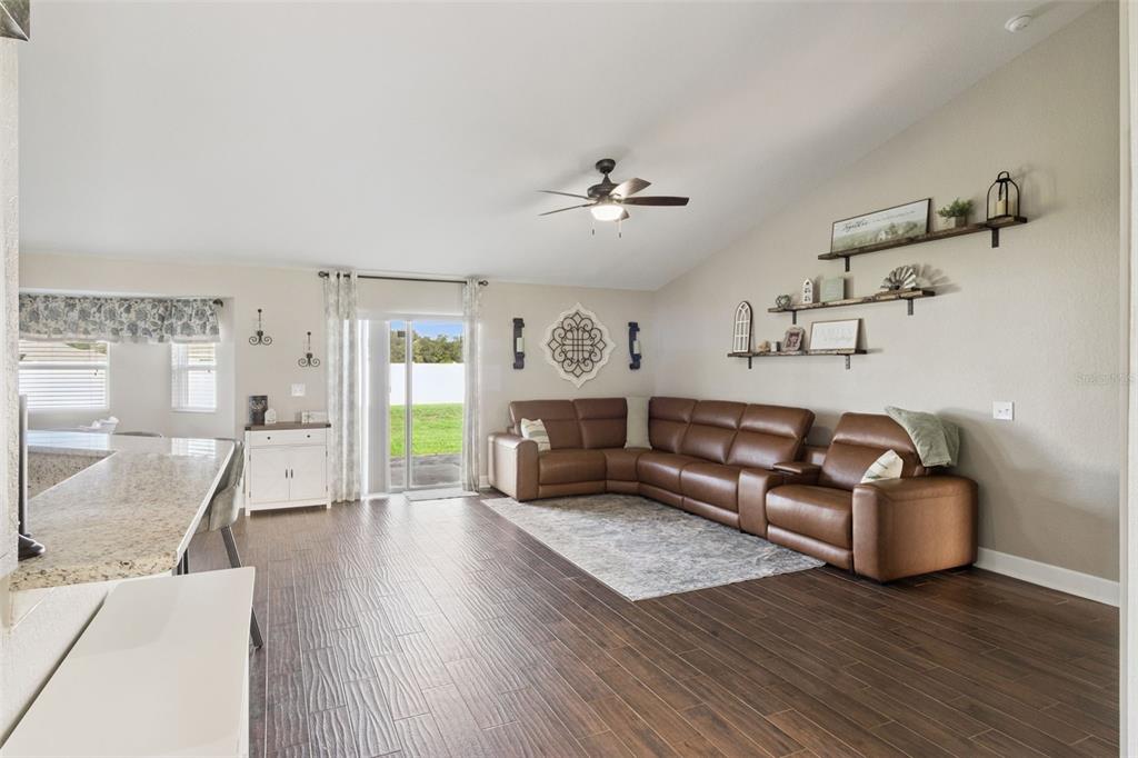 A living room with a brown sectional sofa, wood-look tile floors, and wall-mounted shelves — 925 LOCHLAND LOOP, BARTOW, FL