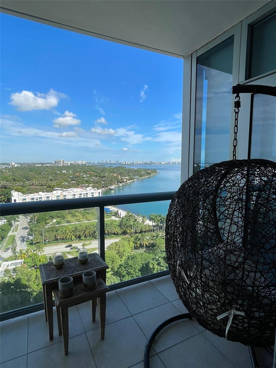 A balcony with a hanging chair, a small wooden table, and a waterfront view — 601 NE 36th St # 1805, Miami FL 33137, MIAMI, FL