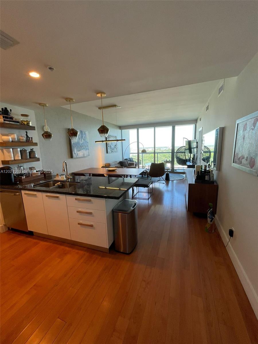 A modern kitchen with white cabinets and granite countertops opens into a bright living area — 601 NE 36th St # 1805, Miami FL 33137, MIAMI, FL