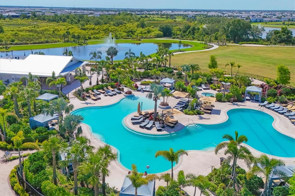 An aerial view of a resort-style swimming pool with palm trees and a nearby pond — 3293 HILLTOP CIRCLE, BRADENTON, FL