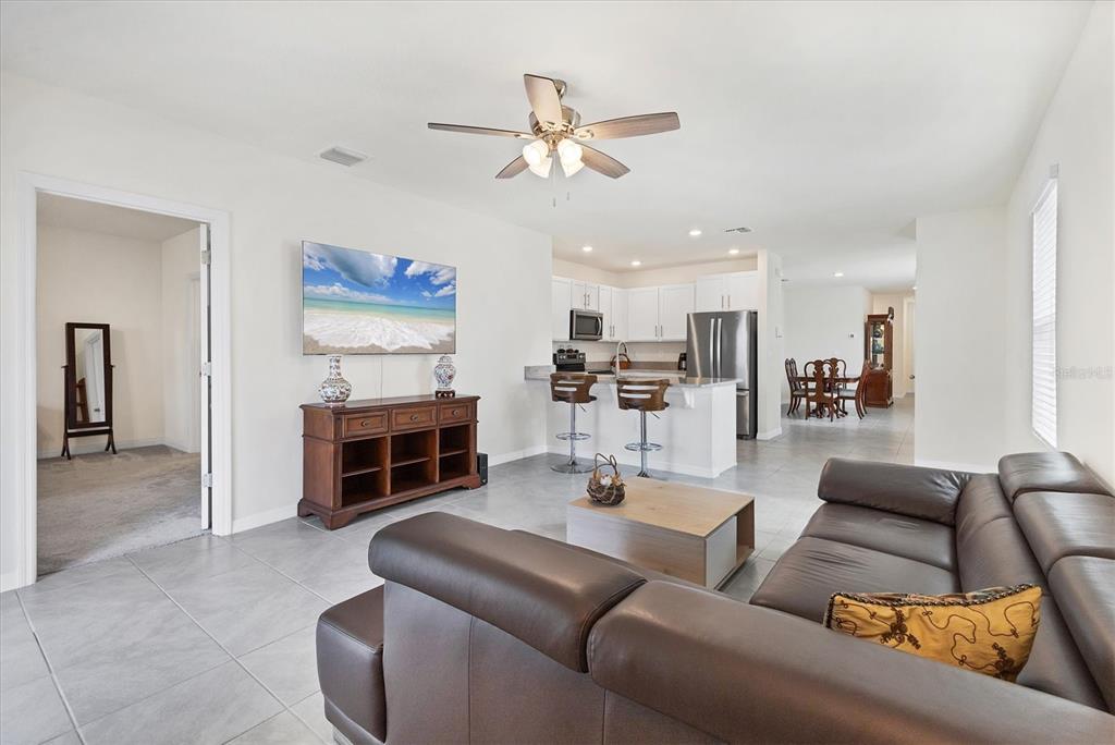 An open-concept living room features tile flooring, a brown leather sofa, and an adjacent kitchen — 3293 HILLTOP CIRCLE, BRADENTON, FL