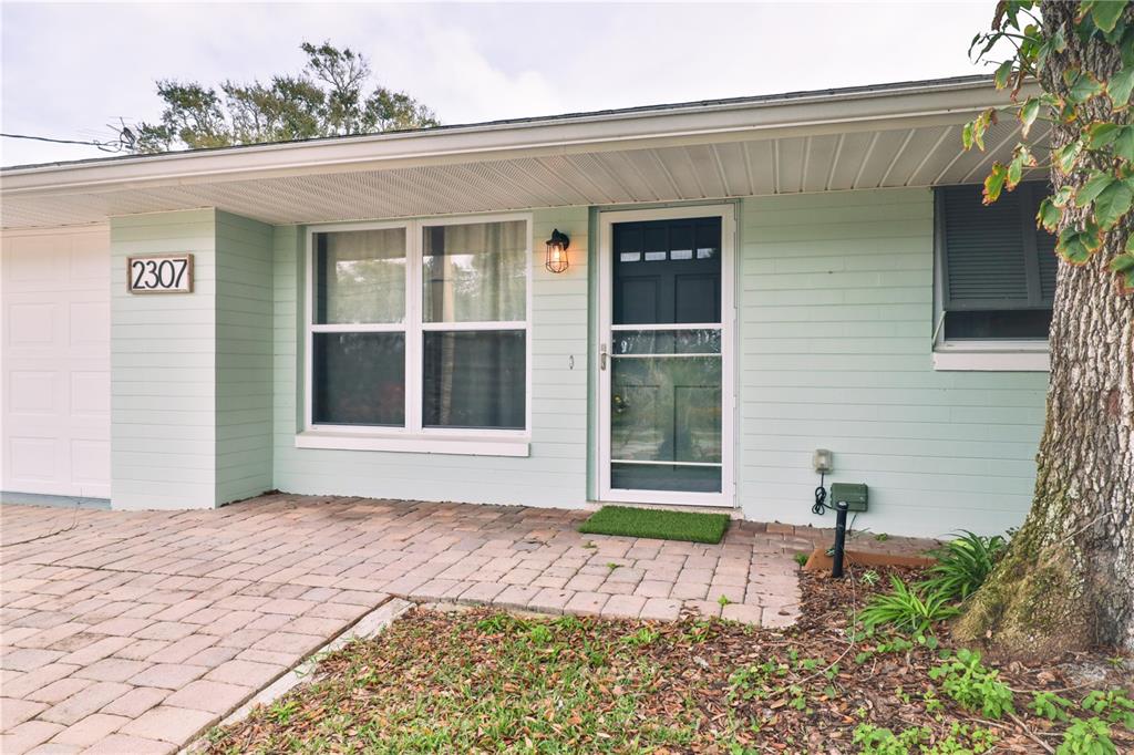 A light green house exterior features a brick paver walkway and a front entry door — 2307 SAXON DRIVE, NEW SMYRNA BEACH, FL