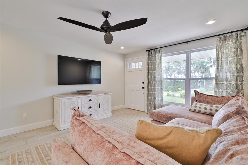 A living room features a pink sectional sofa, a wall-mounted television, and a ceiling fan — 2307 SAXON DRIVE, NEW SMYRNA BEACH, FL