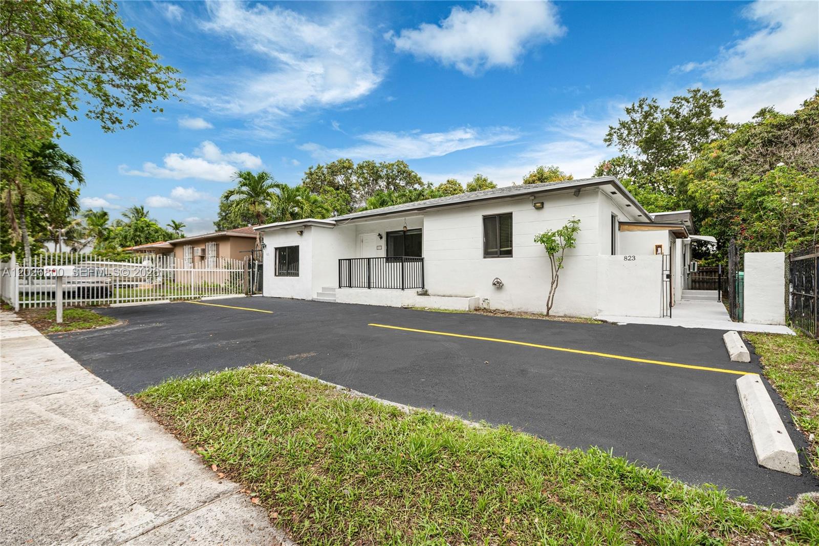 A white single-story house features a paved parking area with yellow lines and concrete bumpers — 821 NW 36th Ave, Miami FL 33125, MIAMI, FL