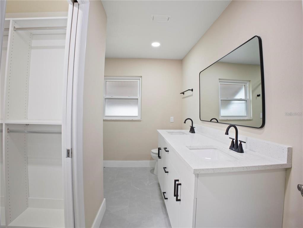 A bathroom features a double vanity with black faucets, a large mirror, and a walk-in closet — 196 W LAKE DAMON DRIVE, AVON PARK, FL