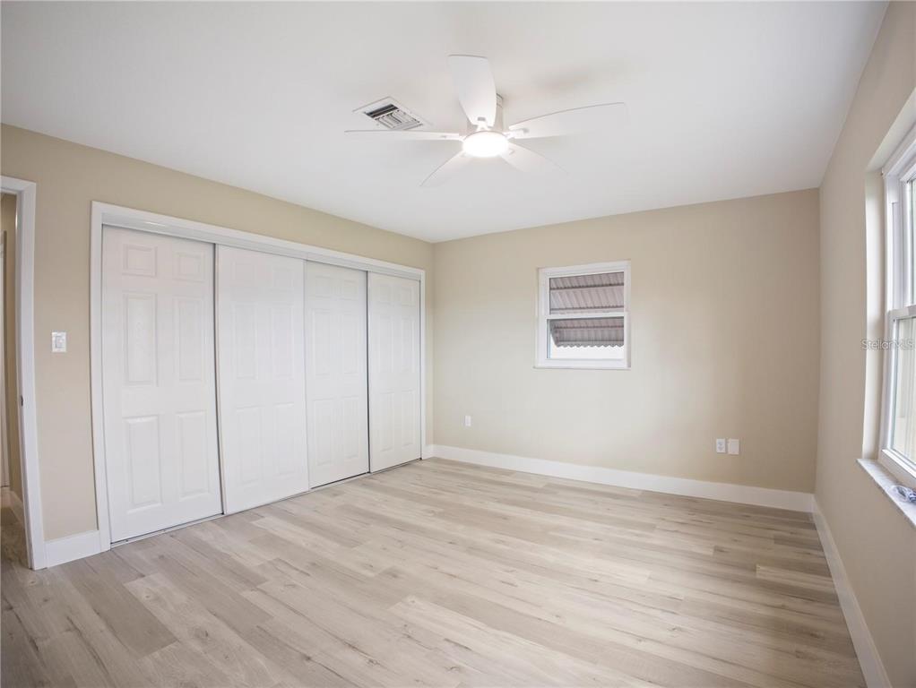 An empty bedroom features light wood-look flooring, beige walls, a ceiling fan, and sliding closet doors — 196 W LAKE DAMON DRIVE, AVON PARK, FL