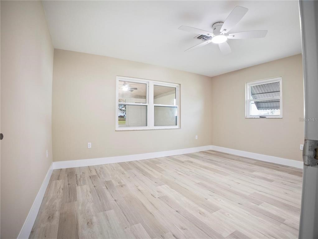 An empty bedroom features light-colored wood-look flooring, beige walls, a ceiling fan, and two windows — 196 W LAKE DAMON DRIVE, AVON PARK, FL