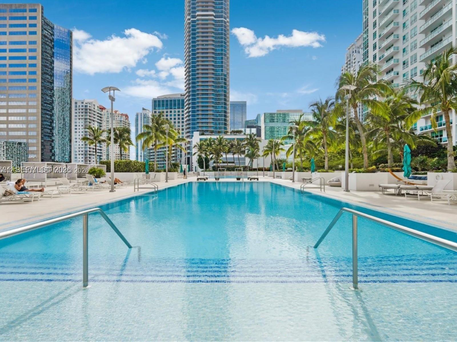 A rectangular swimming pool surrounded by lounge chairs, palm trees, and tall city buildings — 951 Brickell Ave # 1206, Miami FL 33131, MIAMI, FL