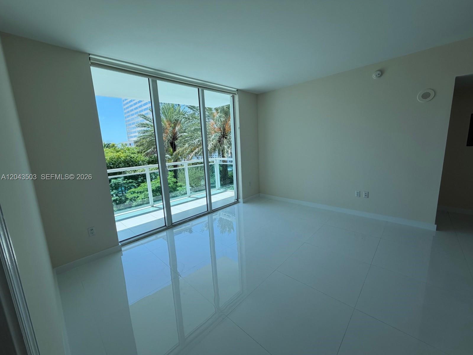 An empty room features white tile flooring, plain walls, and a large sliding glass door — 951 Brickell Ave # 1206, Miami FL 33131, MIAMI, FL