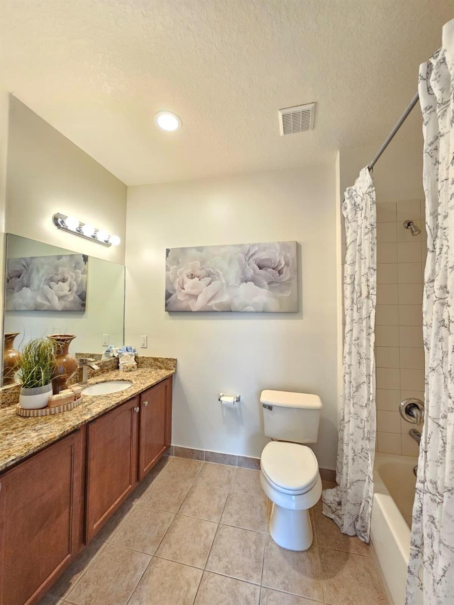 A bathroom features a granite vanity, wooden cabinets, a toilet, and a shower-tub combination — 3022 Laurel Ridge Circle, Riviera Beach FL 33404, RIVIERA BEACH, FL
