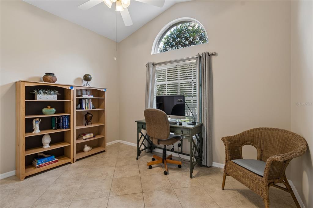 A home office features a desk, two bookcases, a wicker chair, and an arched window — 30600 NICKERSON LOOP, WESLEY CHAPEL, FL