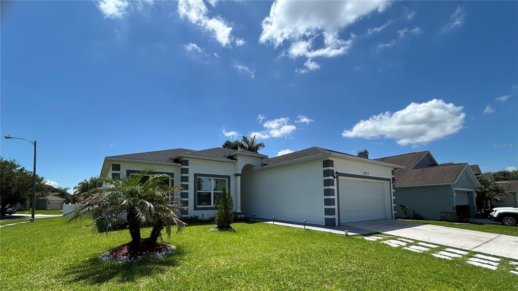 A white single-story house with a two-car garage sits on a corner lot with grass — 2713 WORTHAM LANE, KISSIMMEE, FL