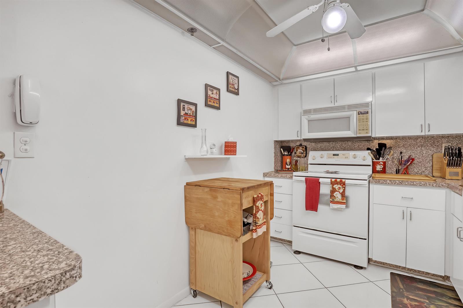 A kitchen with white cabinets, white appliances, a rolling wooden island, and tiled flooring — 3221 S Ocean Boulevard # 1003, Highland Beach FL 33487, HIGHLAND BEACH, FL