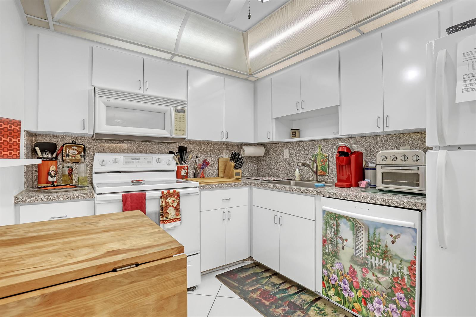 A white kitchen features granite countertops, white cabinetry, and a wooden island in the foreground — 3221 S Ocean Boulevard # 1003, Highland Beach FL 33487, HIGHLAND BEACH, FL