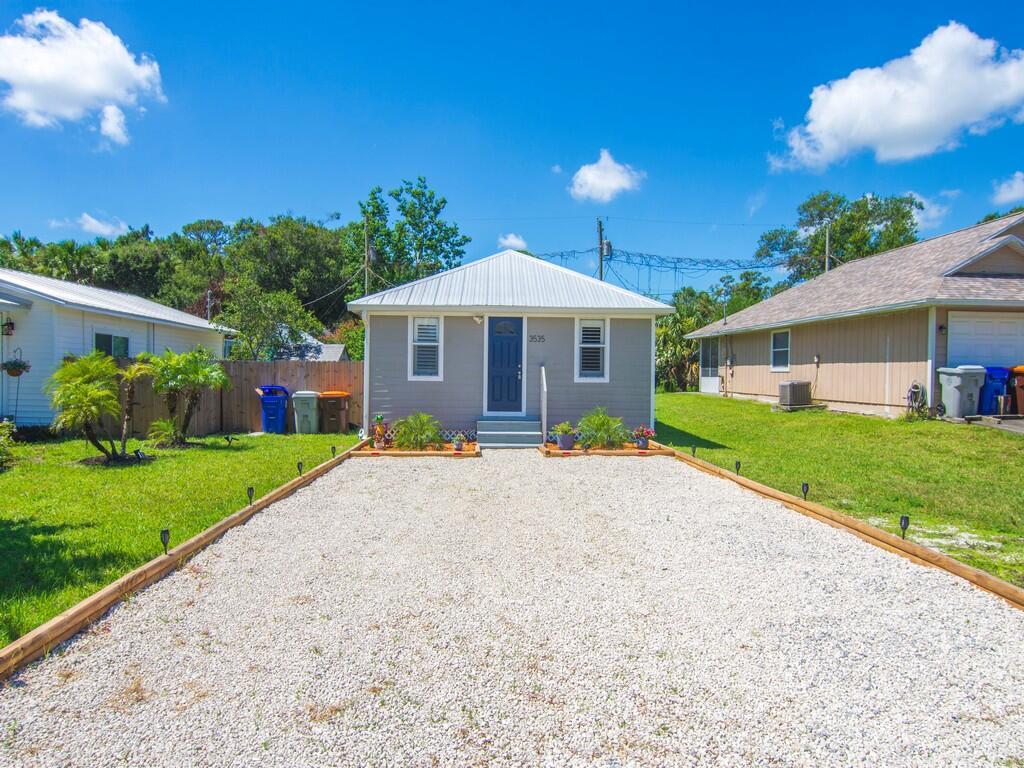 A gray house with a white metal roof features a gravel driveway and front yard — 3535 3rd Street, Vero Beach FL 32968, VERO BEACH, FL