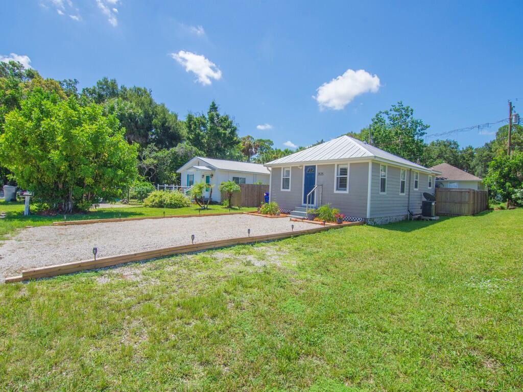 A gray house with a metal roof and a gravel driveway sits on a lawn — 3535 3rd Street, Vero Beach FL 32968, VERO BEACH, FL
