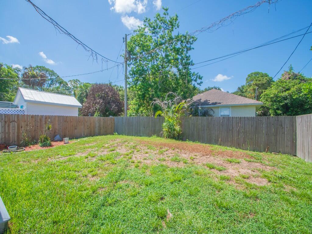 A fenced backyard features a grassy lawn with patches of dirt and surrounding trees — 3535 3rd Street, Vero Beach FL 32968, VERO BEACH, FL