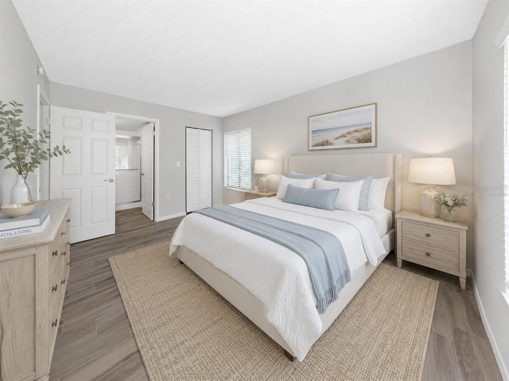 A bedroom features a bed with light blue bedding, wood-look flooring, and a neutral color palette — 3166 LAKE PINE WAY S UNIT H1, TARPON SPRINGS, FL