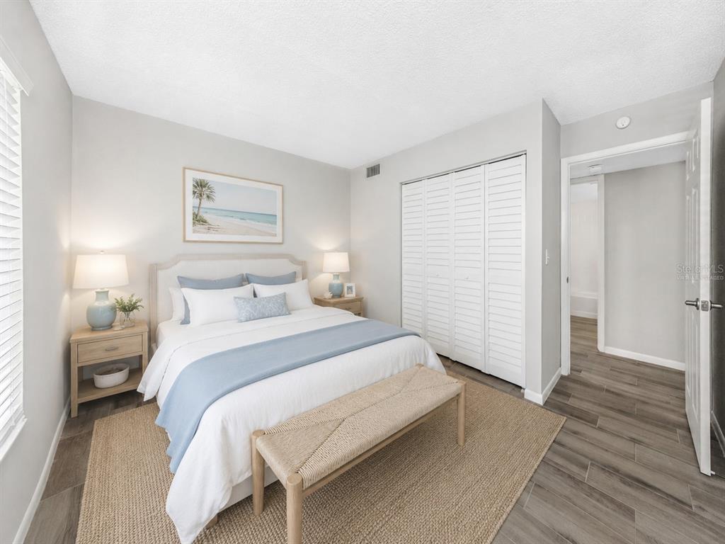 A bedroom features a queen bed, a wooden bench, white louvered closets, and wood-look flooring — 3166 LAKE PINE WAY S UNIT H1, TARPON SPRINGS, FL
