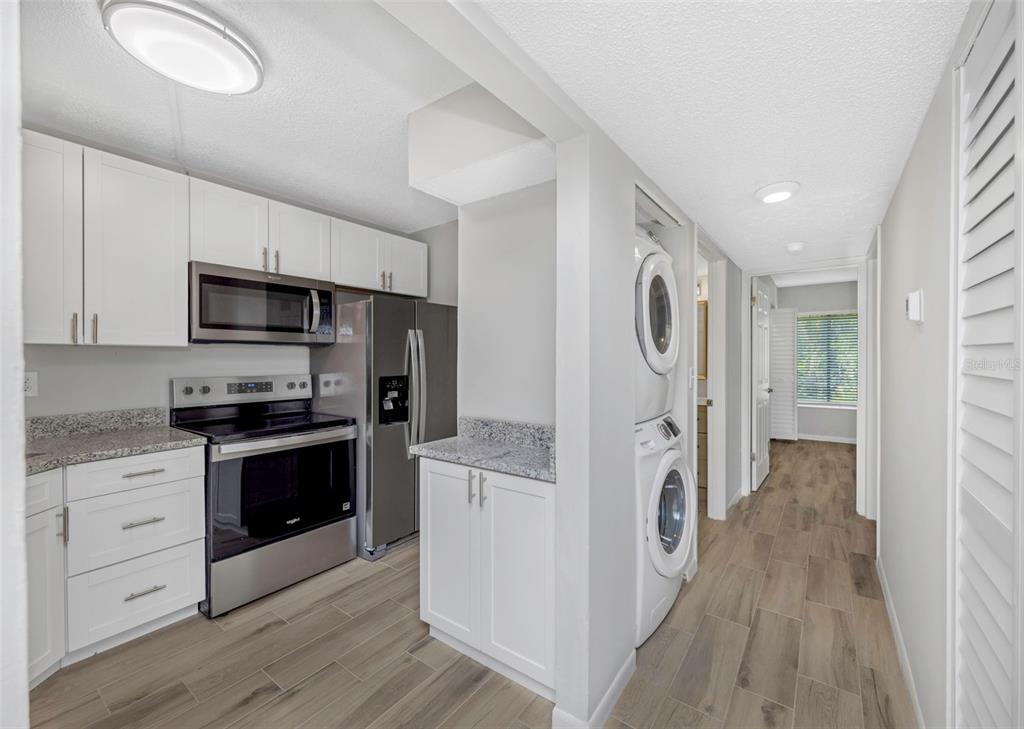 A kitchen with white cabinets, stainless steel appliances, granite countertops, and a stacked laundry unit — 3166 LAKE PINE WAY S UNIT H1, TARPON SPRINGS, FL