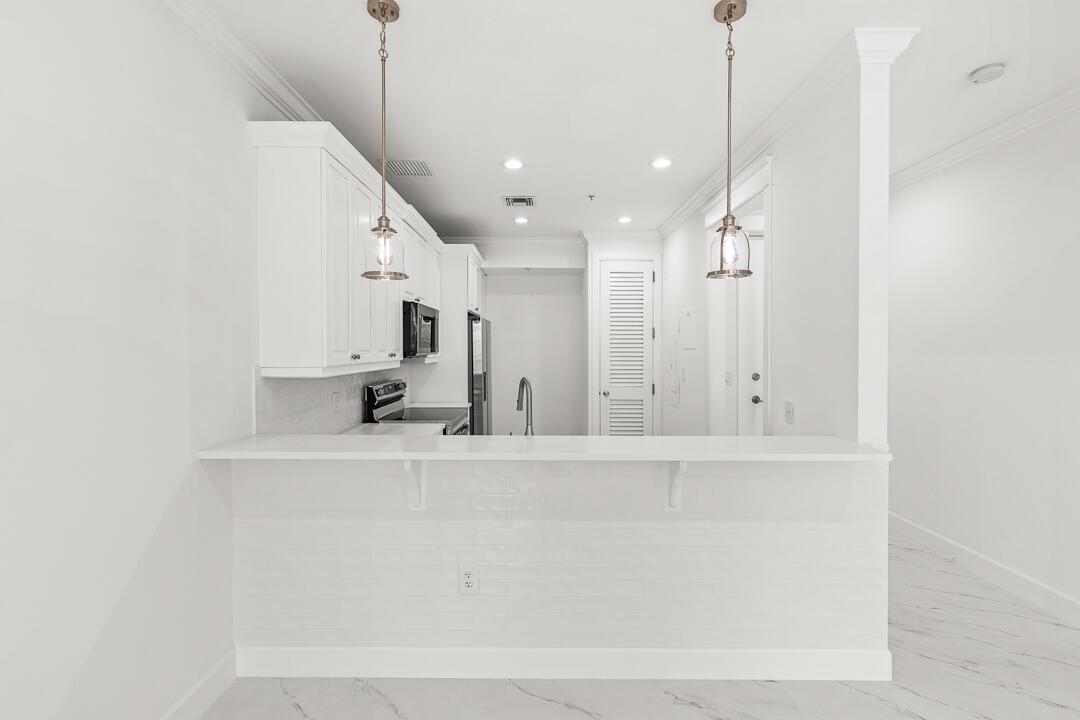 A modern kitchen features white cabinets, stainless steel appliances, and white marble-patterned tile flooring — 47 SW Osceola Street # 206, Stuart FL 34994, STUART, FL