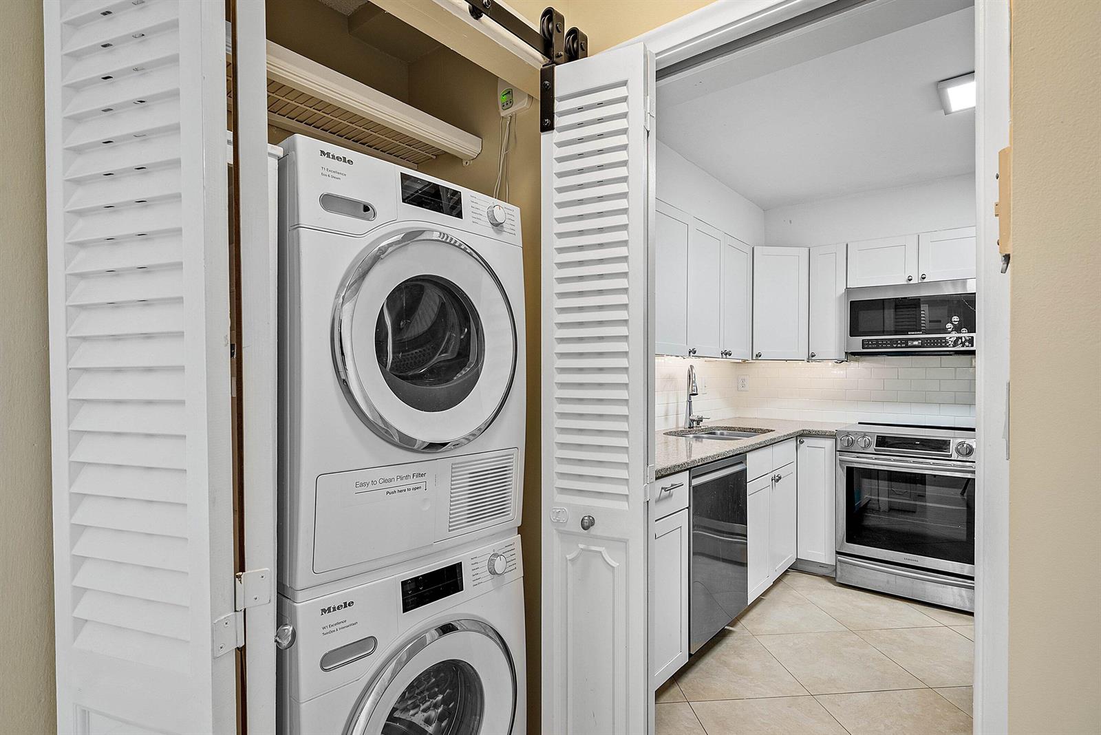 A stacked Miele washer and dryer unit sits in a closet next to a kitchen — 3301 S Ocean Boulevard # 207, Highland Beach FL 33487, HIGHLAND BEACH, FL