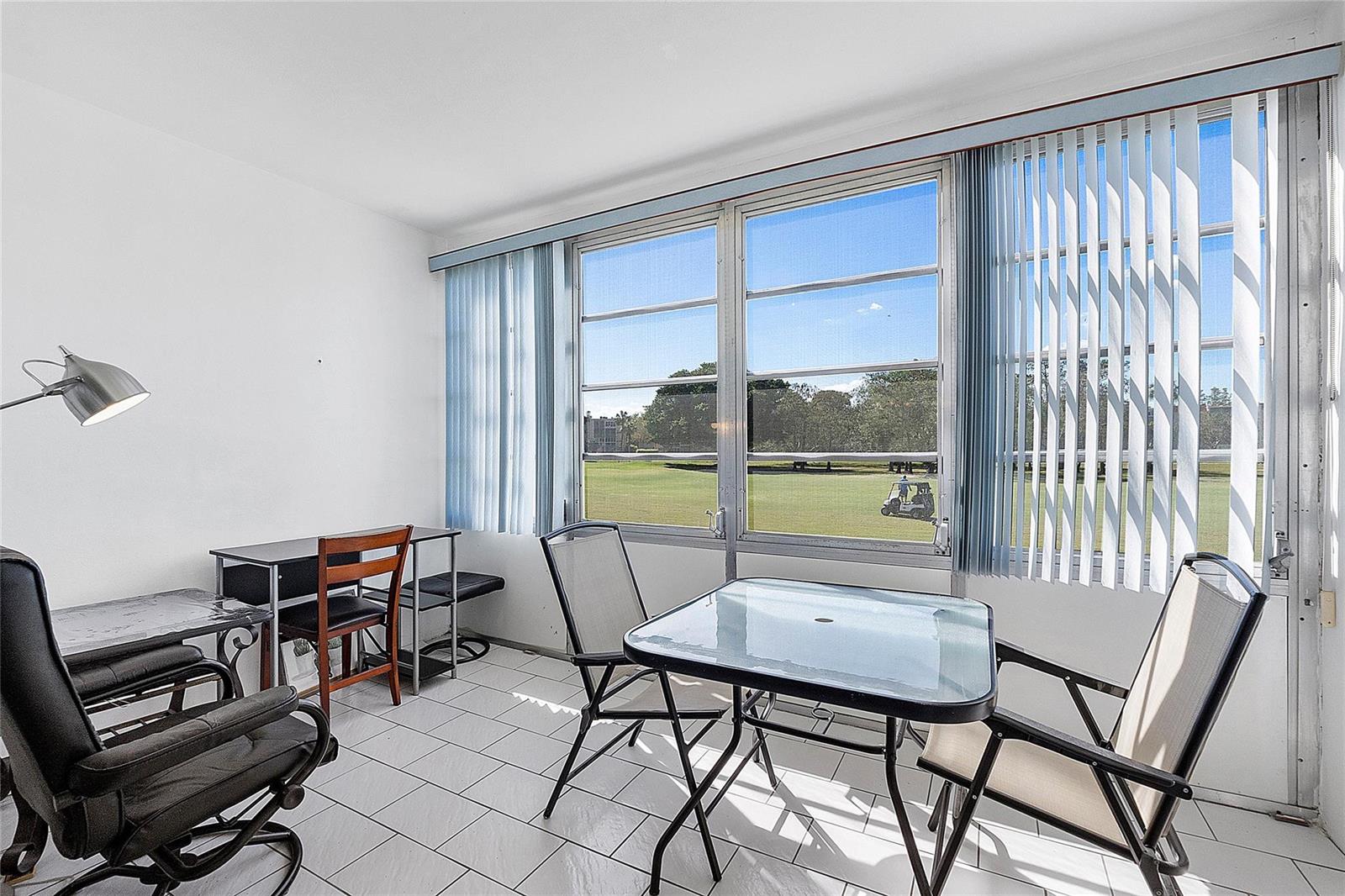 A sunroom with white tile floors, a small dining set, and large windows overlooking a golf course — 7847 Golf Circle Drive # 211, Margate FL 33063, MARGATE, FL