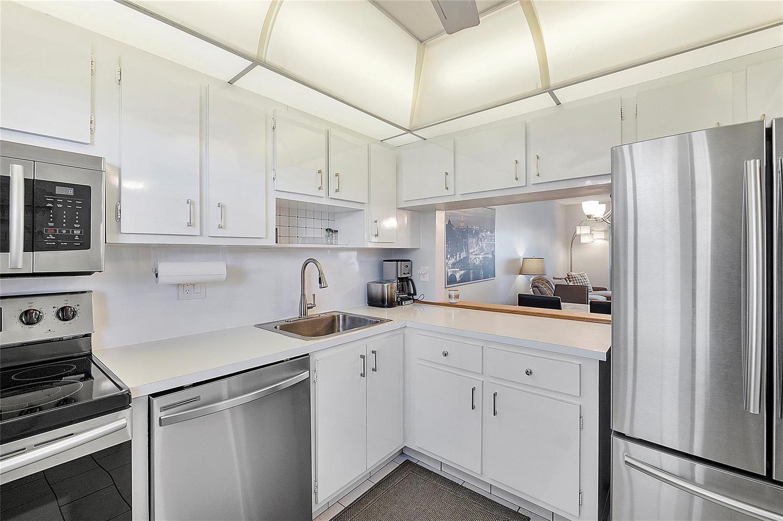 A kitchen with white cabinets, stainless steel appliances, and a pass-through window to the living area — 7847 Golf Circle Drive # 211, Margate FL 33063, MARGATE, FL