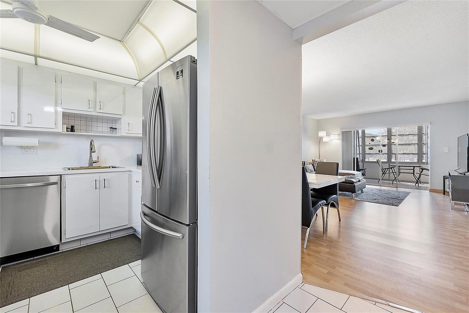 A kitchen with stainless steel appliances opens into a living area with wood-look flooring — 7847 Golf Circle Drive # 211, Margate FL 33063, MARGATE, FL
