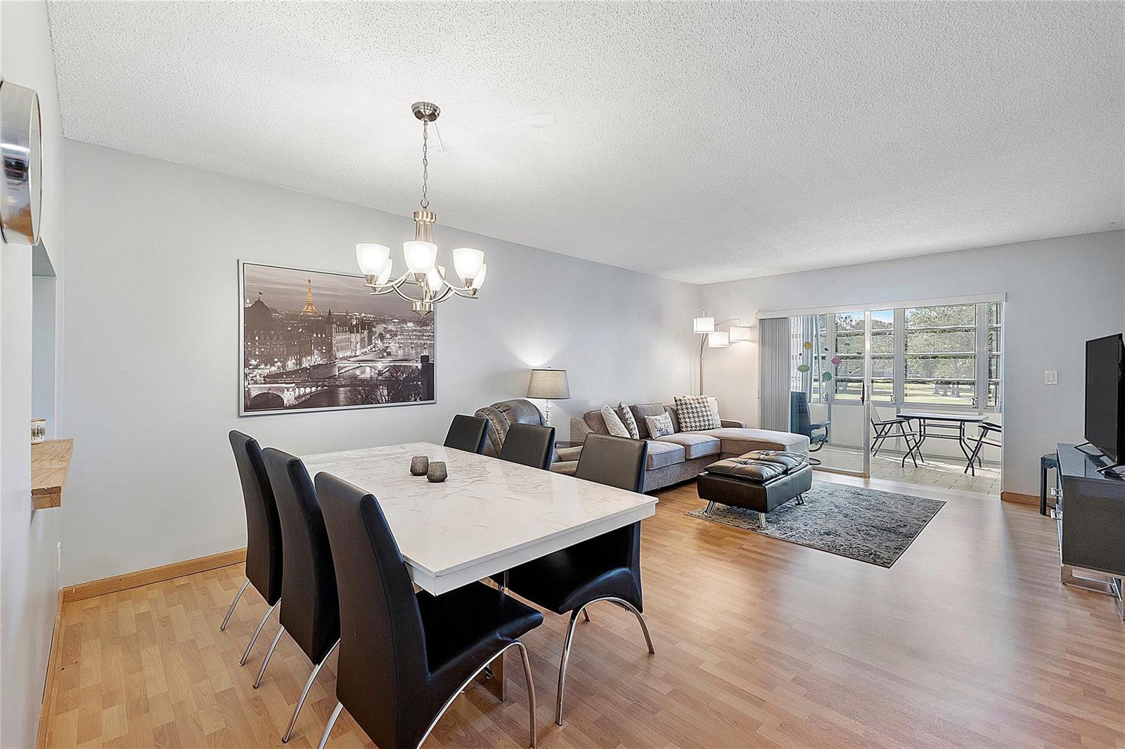 An open-concept living and dining room features light wood flooring, a marble-topped table, and balcony — 7847 Golf Circle Drive # 211, Margate FL 33063, MARGATE, FL