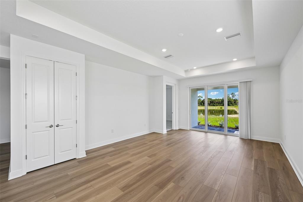 An empty room with white walls, wood-look flooring, a tray ceiling, and sliding glass doors — 9669 CRYSTAL ISLES CIRCLE, SARASOTA, FL