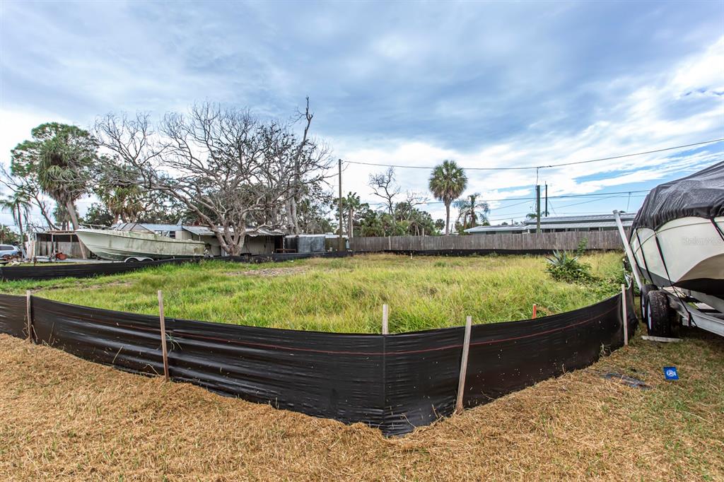A vacant, grassy residential lot is enclosed by black silt fencing with boats parked nearby — 6813 GARDEN DRIVE, NEW PORT RICHEY, FL