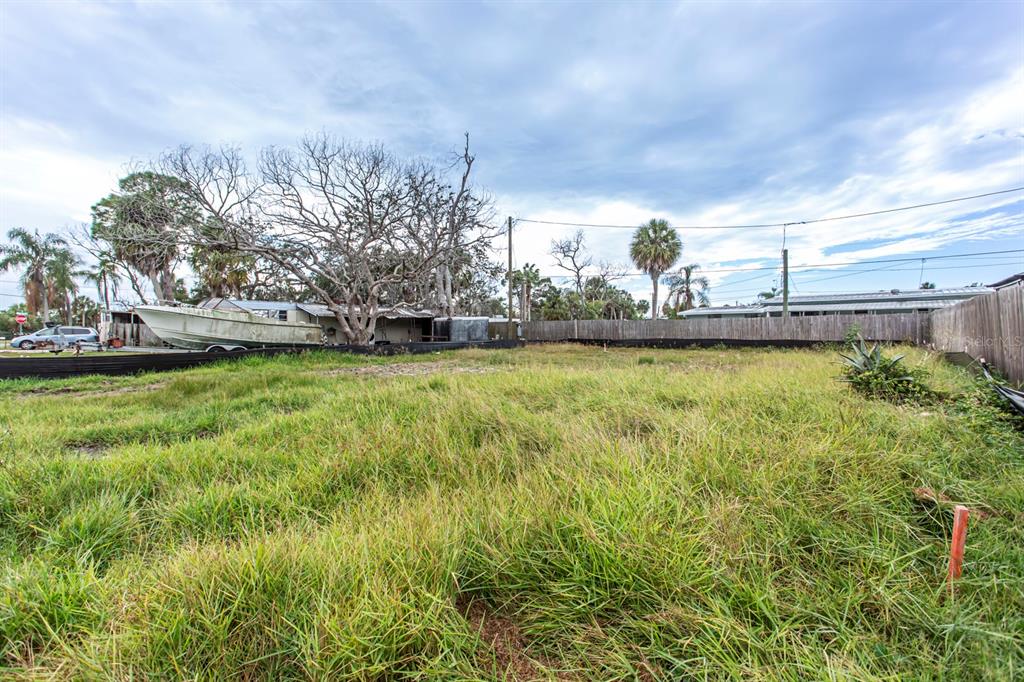 A vacant, grassy lot features a boat parked in the background behind a wooden fence — 6813 GARDEN DRIVE, NEW PORT RICHEY, FL