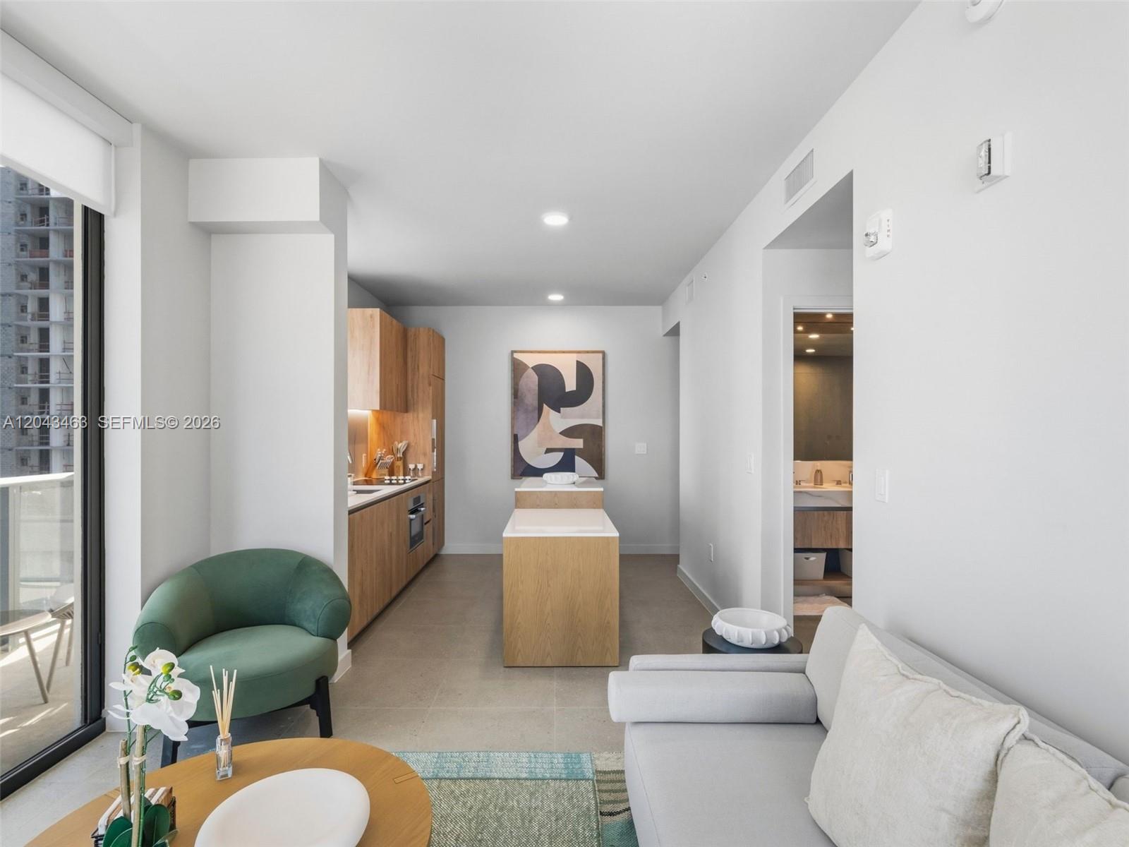 A modern kitchen with light wood cabinetry and a central island sits beside a living area — 11 NE 6th St # 1509, Miami FL 33132, MIAMI, FL