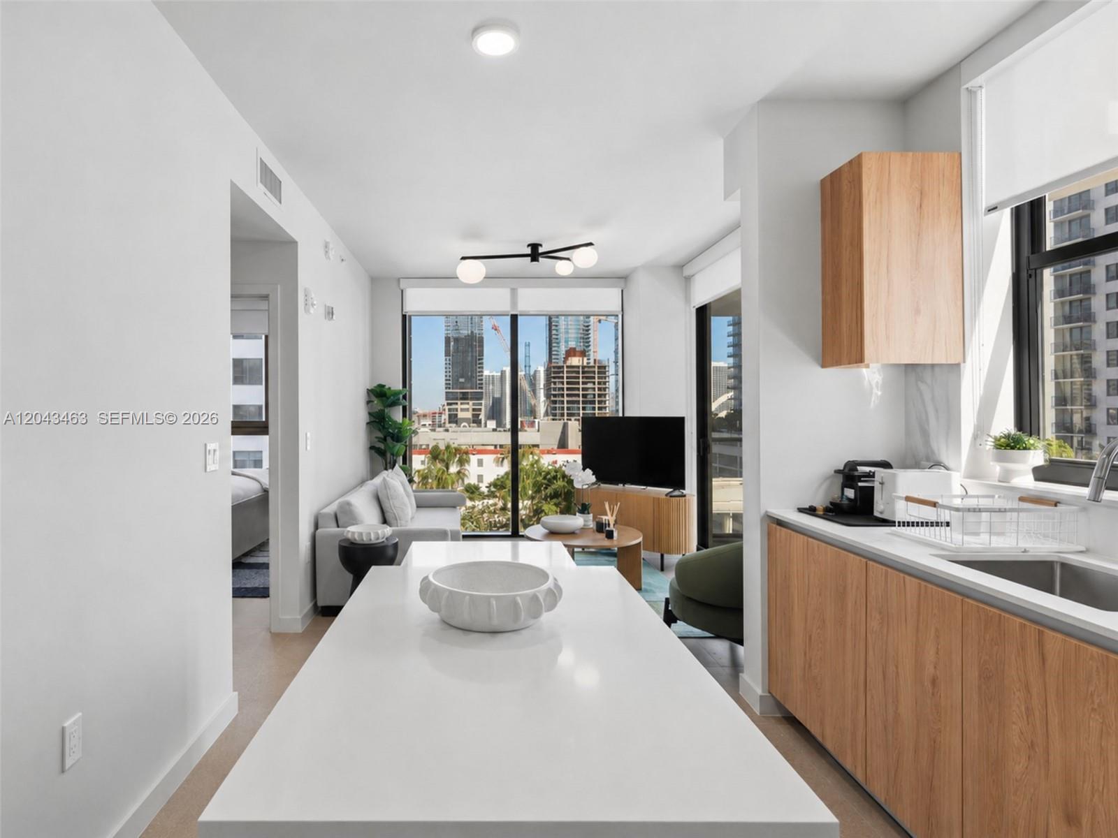 A modern kitchen island overlooks a living area with floor-to-ceiling windows and city views — 11 NE 6th St # 1509, Miami FL 33132, MIAMI, FL