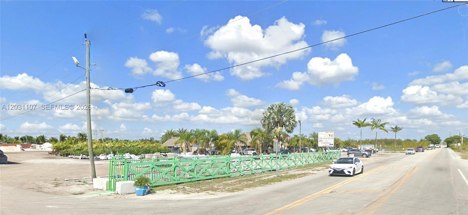 A green fence borders a gravel lot with palm trees and a white car — 19000 SW 137th Ave, Miami FL 33177, MIAMI, FL