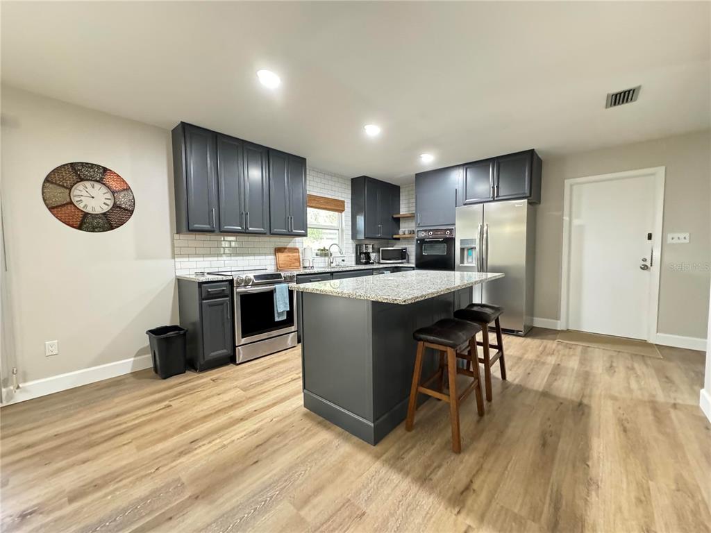 A kitchen features dark gray cabinets, stainless steel appliances, a granite island, and wood flooring — 1836 NW 40TH TERRACE, GAINESVILLE, FL