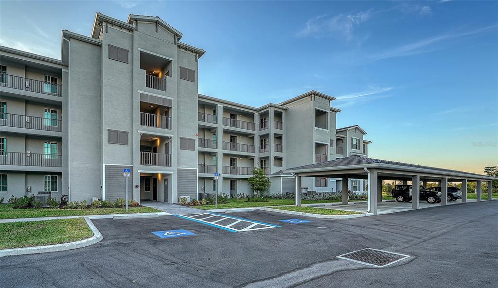 A multi-story apartment building with a covered parking structure and accessible parking spaces in front — 17655 OPAL SAND DRIVE UNIT 302, VENICE, FL