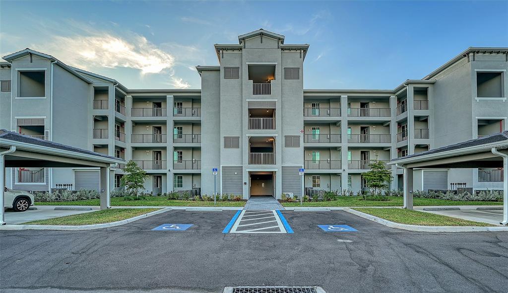 A multi-story apartment building exterior features a central entrance, covered parking, and accessible parking spaces — 17655 OPAL SAND DRIVE UNIT 302, VENICE, FL